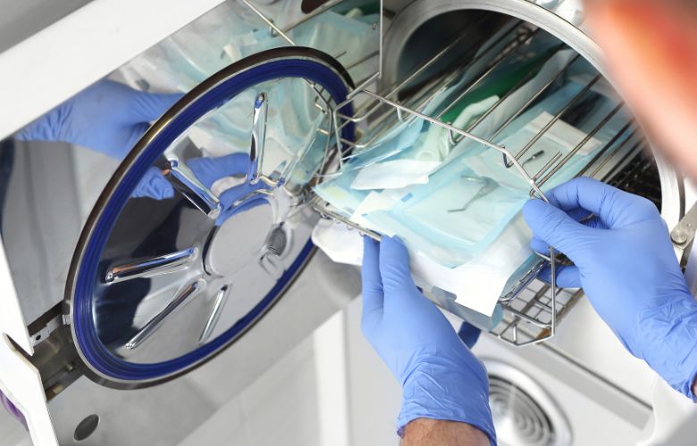 Sterilisation von medizinischen Instrumenten in einem Autoklaven durch eine Person mit blauen Handschuhen.